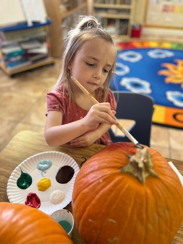 a girl is painting a pumpkin with a brush at Mrs. B's Day Care Too 